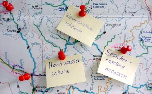 Ausschnitt einer Bayernkarte, auf dem drei Notizzettel festgepinnt sind. Diese tragen von links  nach rechts die Aufschriften:  Hochwasserschutz, Wärmeeinleitung reduzieren und Speicherregelung anpassen.